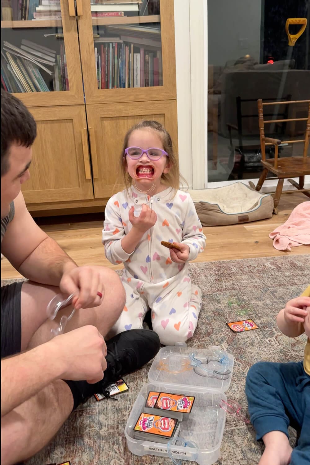 Board Game Storage Ideas in real life, showing family game night playing Watch Your Mouth with the mouthpiece and cards stored in a labeled plastic case for easy, stackable game storage.