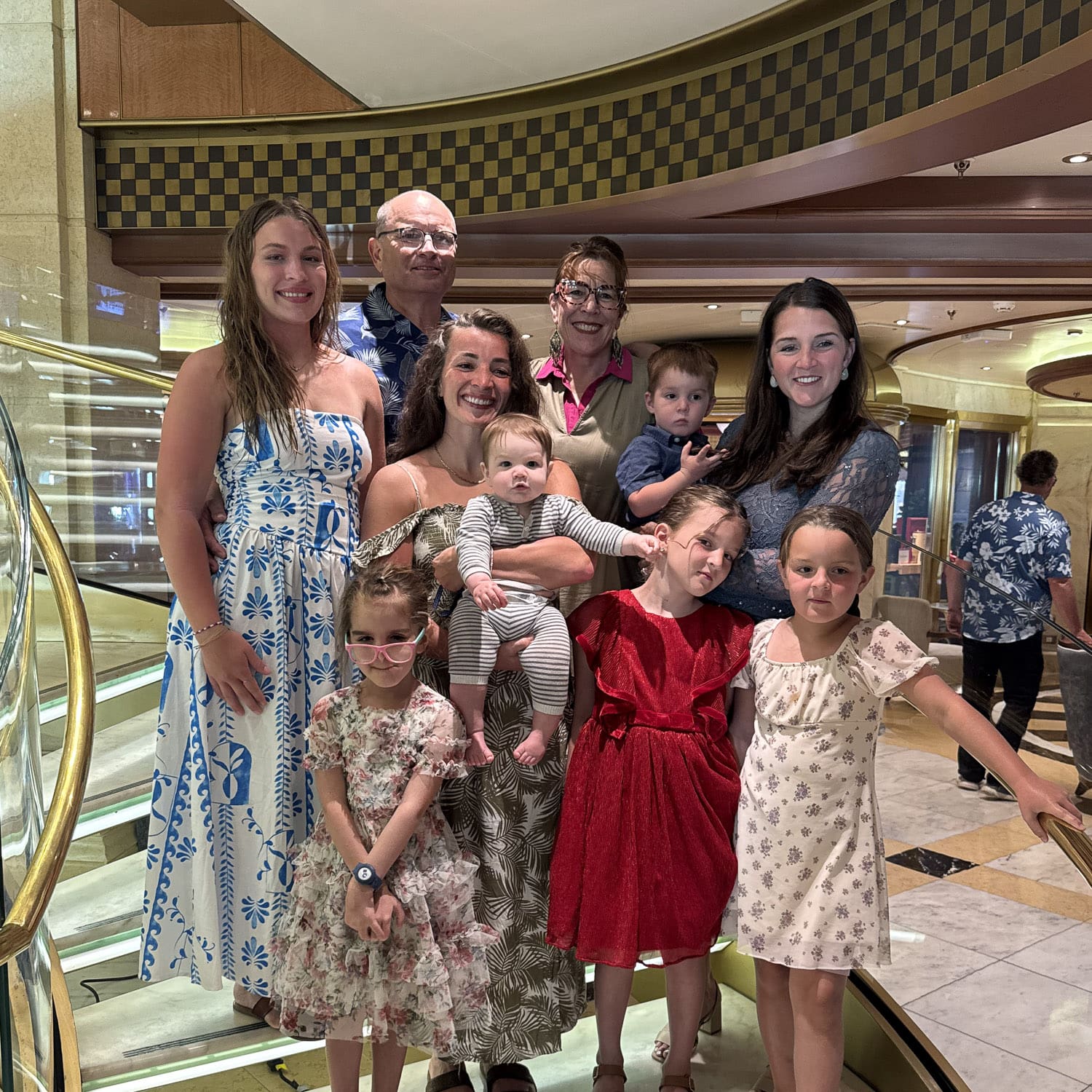 Big family group photo on a Princess cruise ship staircase during formal night, with adults and kids in dressy outfits and a baby in a striped onesie.