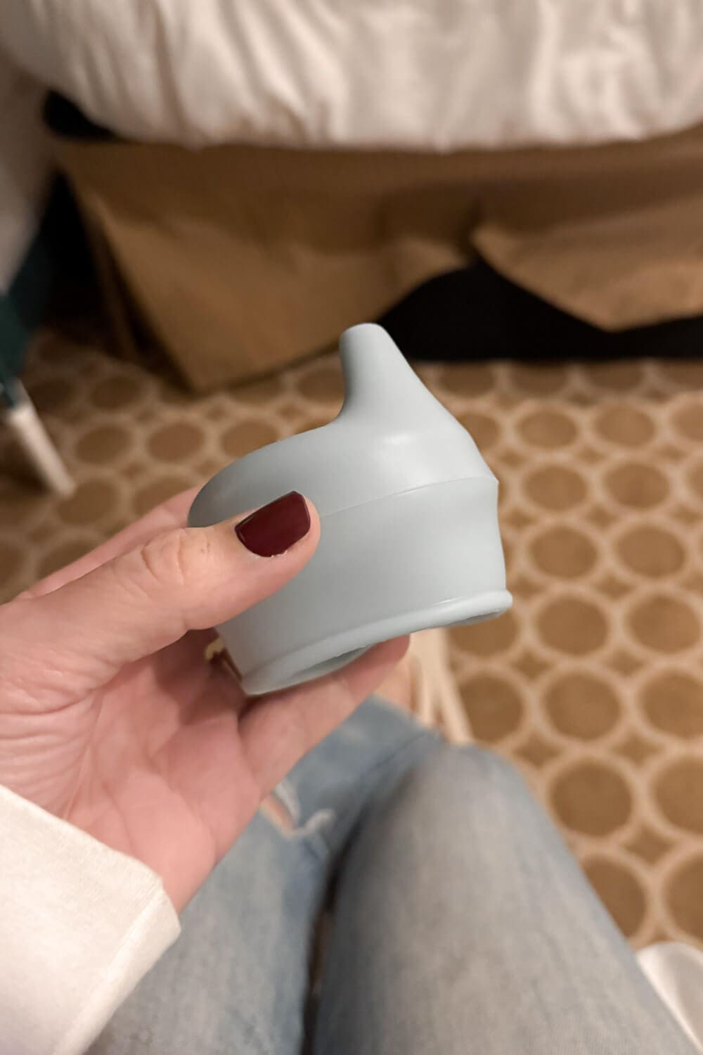 Close-up of a hand holding a silicone sippy cup lid topper inside a ship's cabin, a simple travel with children packing essential for turning regular cups into spill-resistant cups.