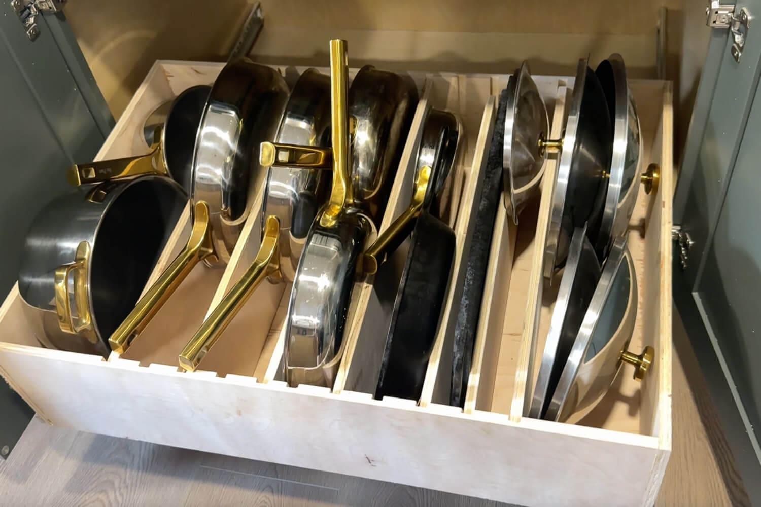 Custom slide-out pots and pans storage drawer organizer with wood dividers keeping frying pans, saucepans, and lids stored upright inside a lower kitchen cabinet.