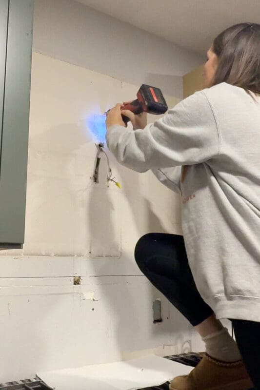 DIYer standing on the stovetop using an oscillating multi-tool to cut drywall for a new electrical box.