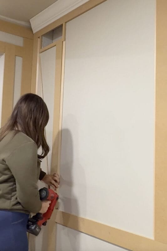 Attaching thin picture frame molding inside the box molding panels with a brad nailer to create a layered, custom wall trim look.