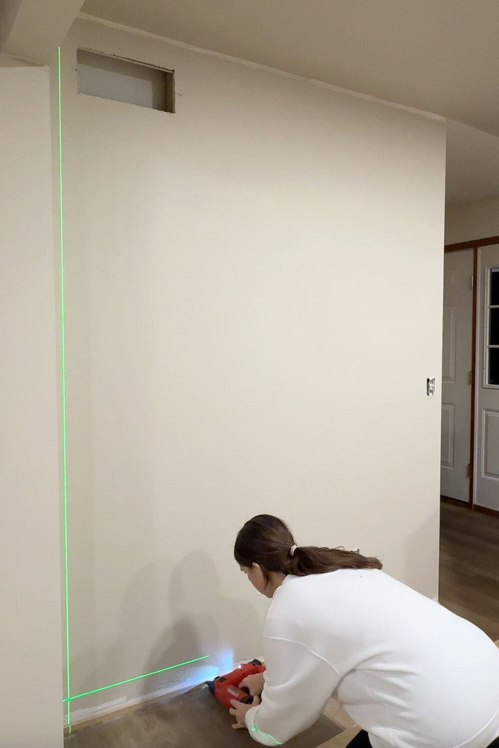 Attaching the lower trim board for DIY wall trim work with a brad nailer while lining everything up with a laser level.