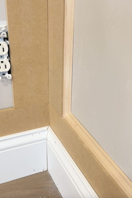 Finished corner detail of DIY box molding wall trim with layered inner molding, showing clean lines around the baseboard and wall panel.