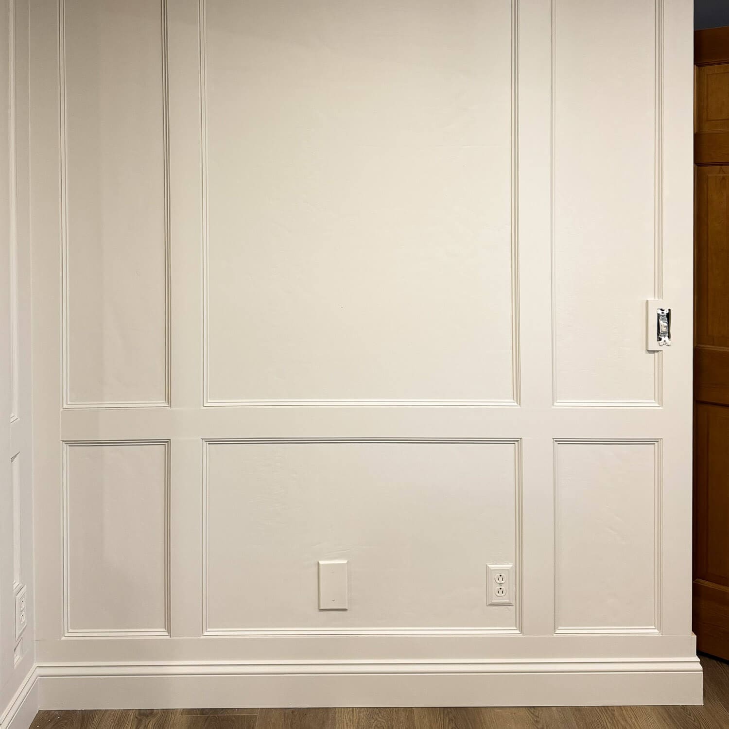 Close-up of DIY box molding wall trim showing the chair rail and lower picture frame panels around an outlet and wall plate.