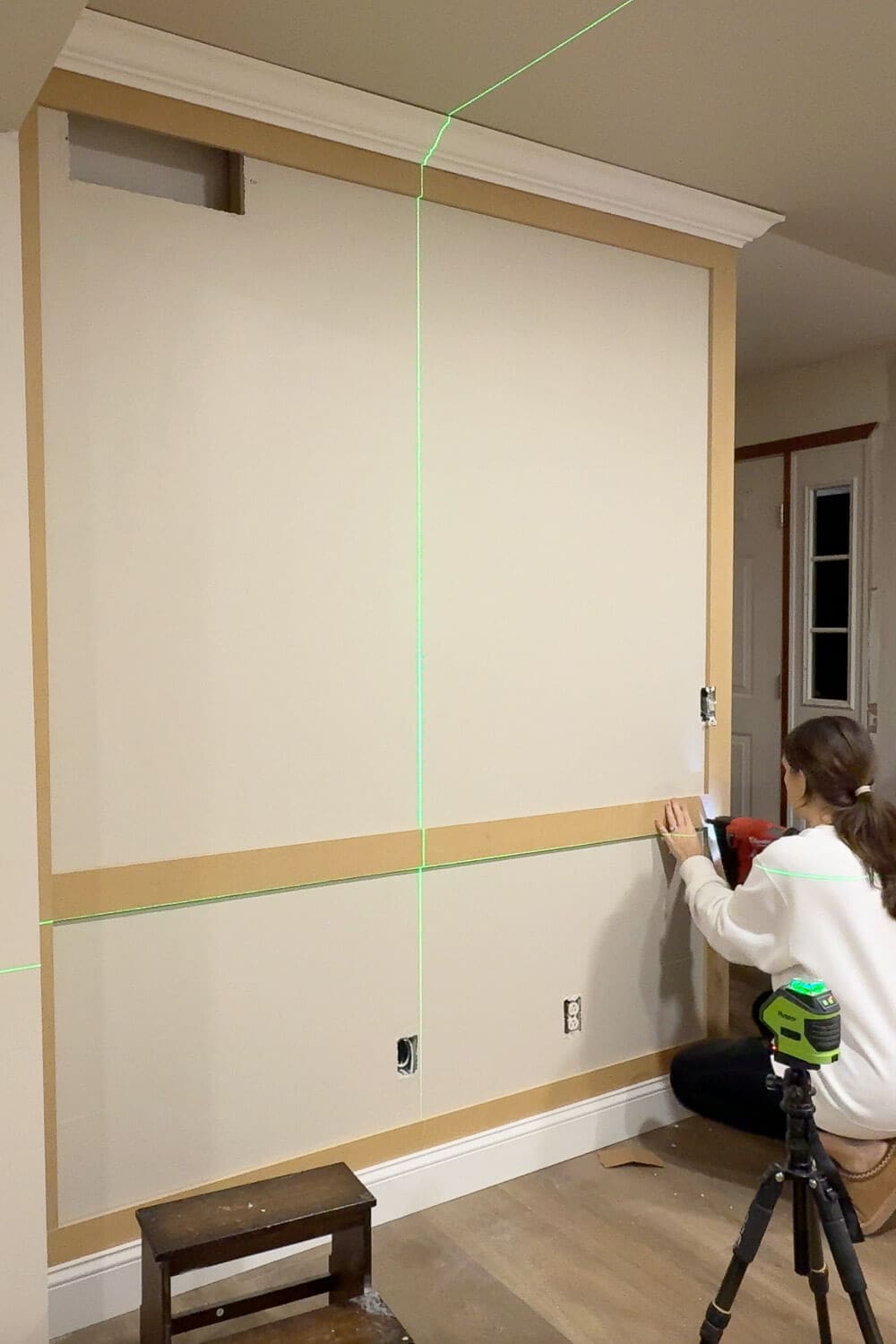 Installing the center chair rail panel picture frame wall trim using a green laser level for straight, even panel spacing.