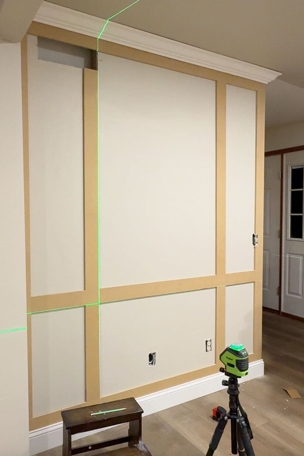 DIY box molding wall trim layout with large and narrow panels marked out, using a green laser level to keep the grid straight before finishing.