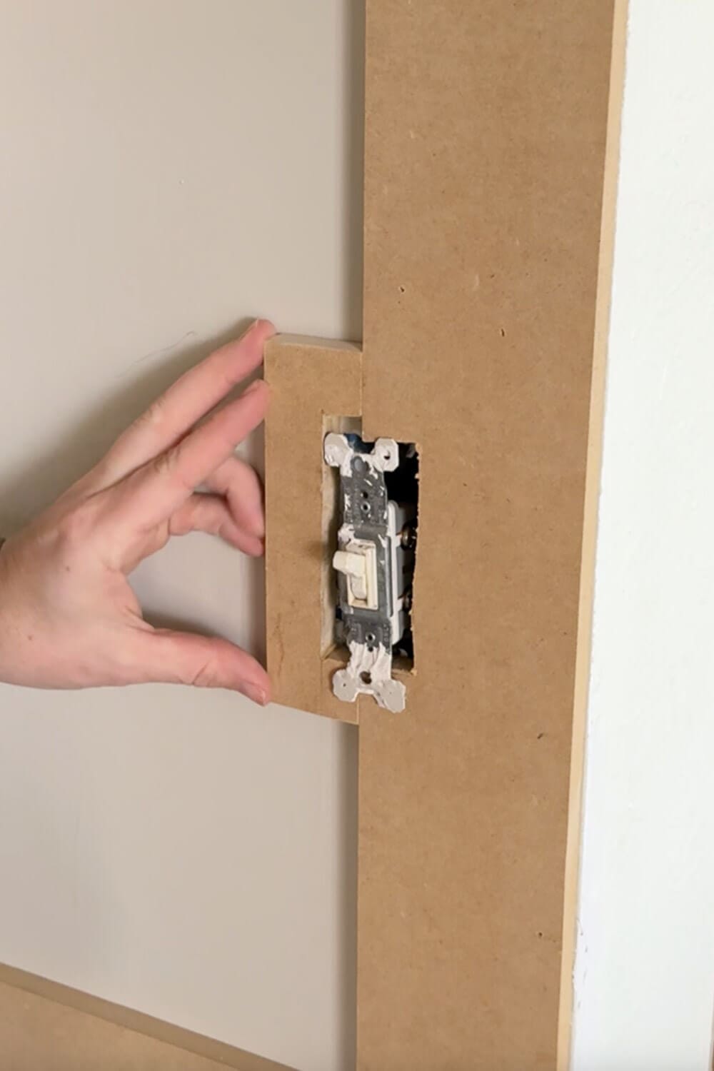 Notching a DIY box molding wall trim board to fit around a light switch, showing how to work around electrical boxes during wall panel installation.