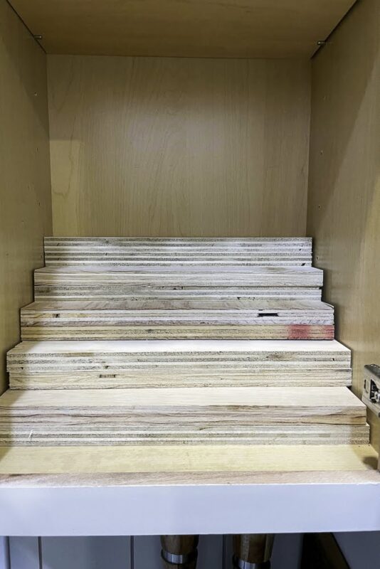 Cut wood pieces stacked inside a cabinet, prepped to build a DIY tiered spice rack for better spice cabinet storage.