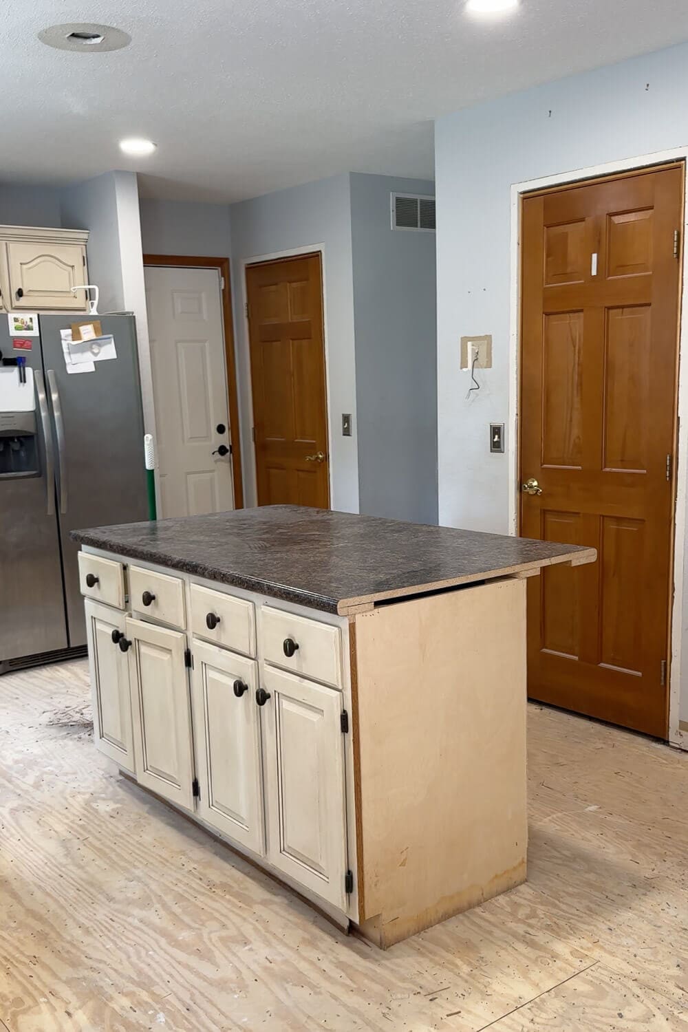 Kitchen before renovation showing the side closet and pantry next to the old peninsula cabinets turned temporary island, with flooring removed down to the subfloor.