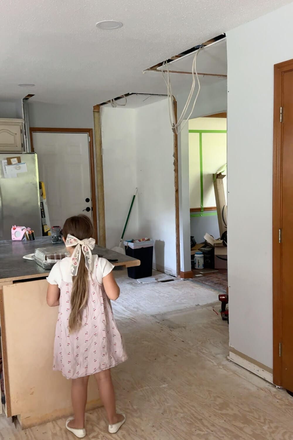 Same kitchen view after demo with the closet and pantry removed, drywall and ceiling opened up with exposed wiring, and the space opened up around the temporary island during renovation.