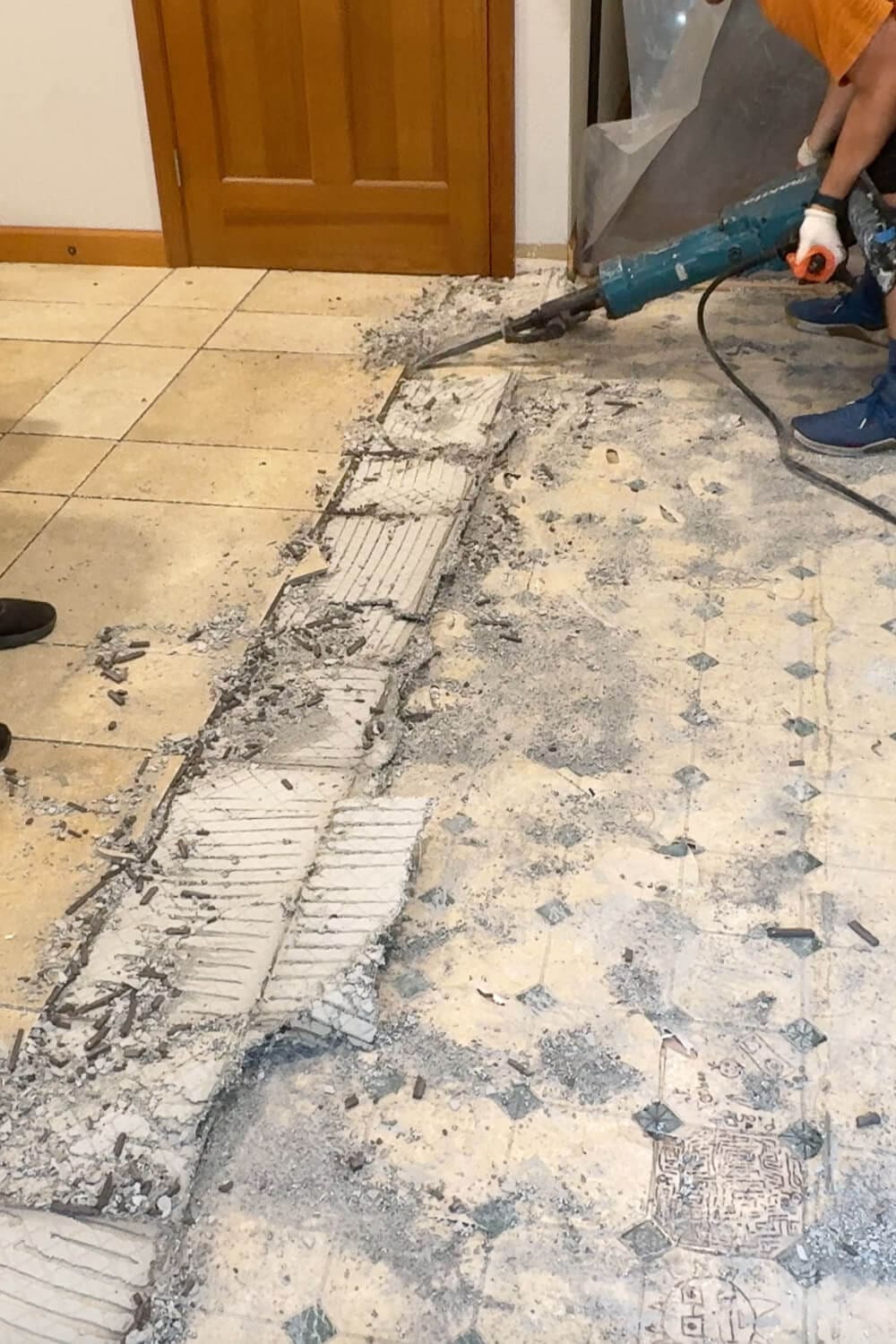 Using a demolition hammer to break up old tile and thinset, leaving a dusty strip of exposed old linoleum.