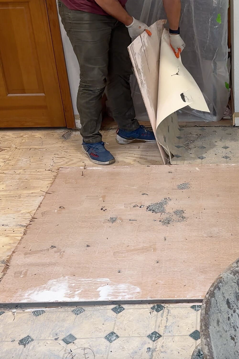 Rolling up the old sheet vinyl flooring during kitchen demo, showing the transition from patterned vinyl to bare subfloor as the flooring gets removed.