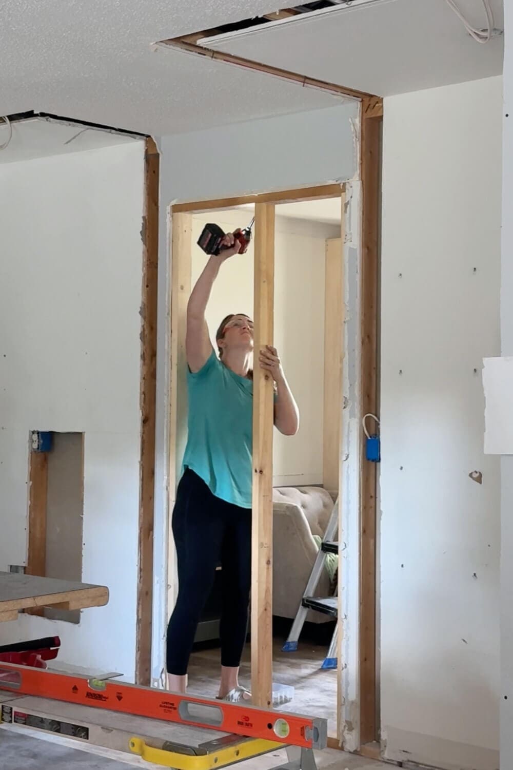 Framing in the old opening between the kitchen and dining room with studs and a drill, closing it off to prep for a new cabinet wall.