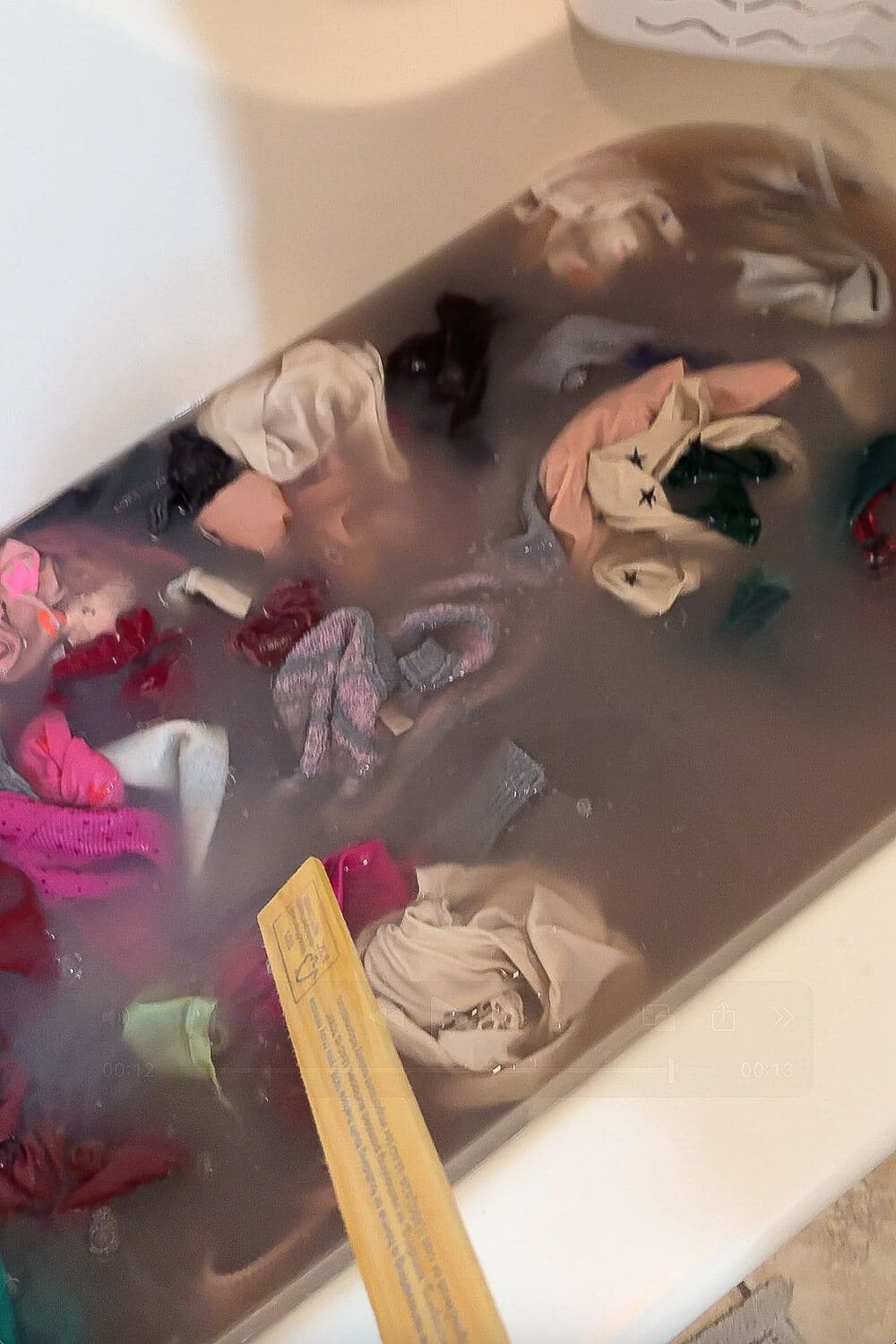 Bathtub filled with hot water and clothes soaking during laundry stripping, showing cloudy gray water from detergent buildup and odors lifting out.