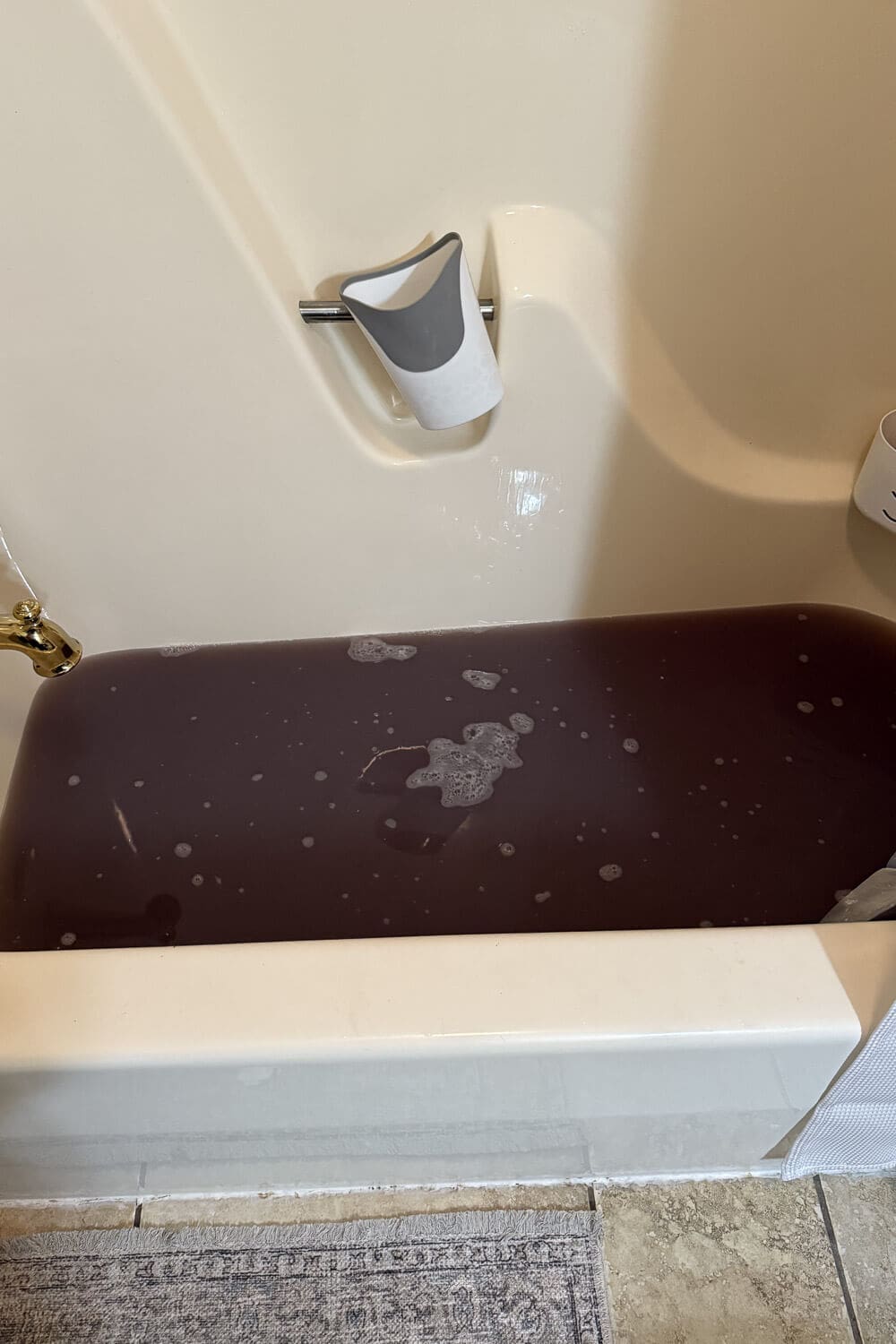 Bathtub filled with dark, murky water after laundry stripping, showing gross detergent buildup and grime pulled out of clothes during a deep clean soak.