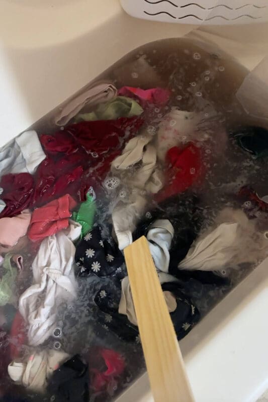 Bathtub full of clothes soaking in laundry stripping solution with murky water and bubbles as buildup and odors get pulled out.