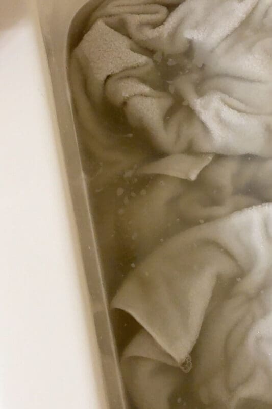 Close-up of white towels in a laundry stripping bath as the water turns yellow-brown from built-up gunk and trapped odors lifting out.