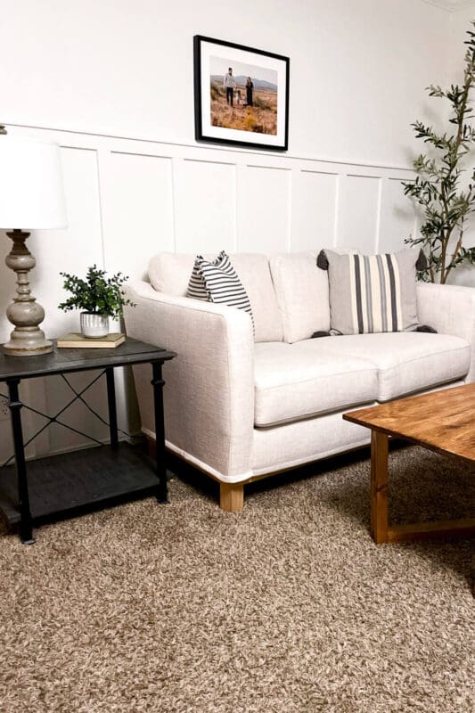 Finished living room wall molding accent wall painted white behind a light sofa, showing vertical panel trim with cozy neutral styling.