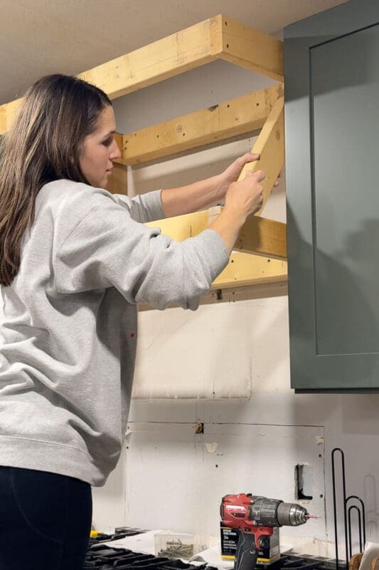 Marking the angle on a 2x4 to cut an angled support brace for the DIY range hood cover frame.
