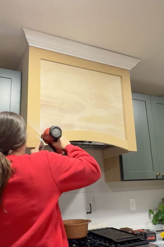 I use a nail gun to secure the curved bottom trim piece onto the front of the DIY range hood cover.