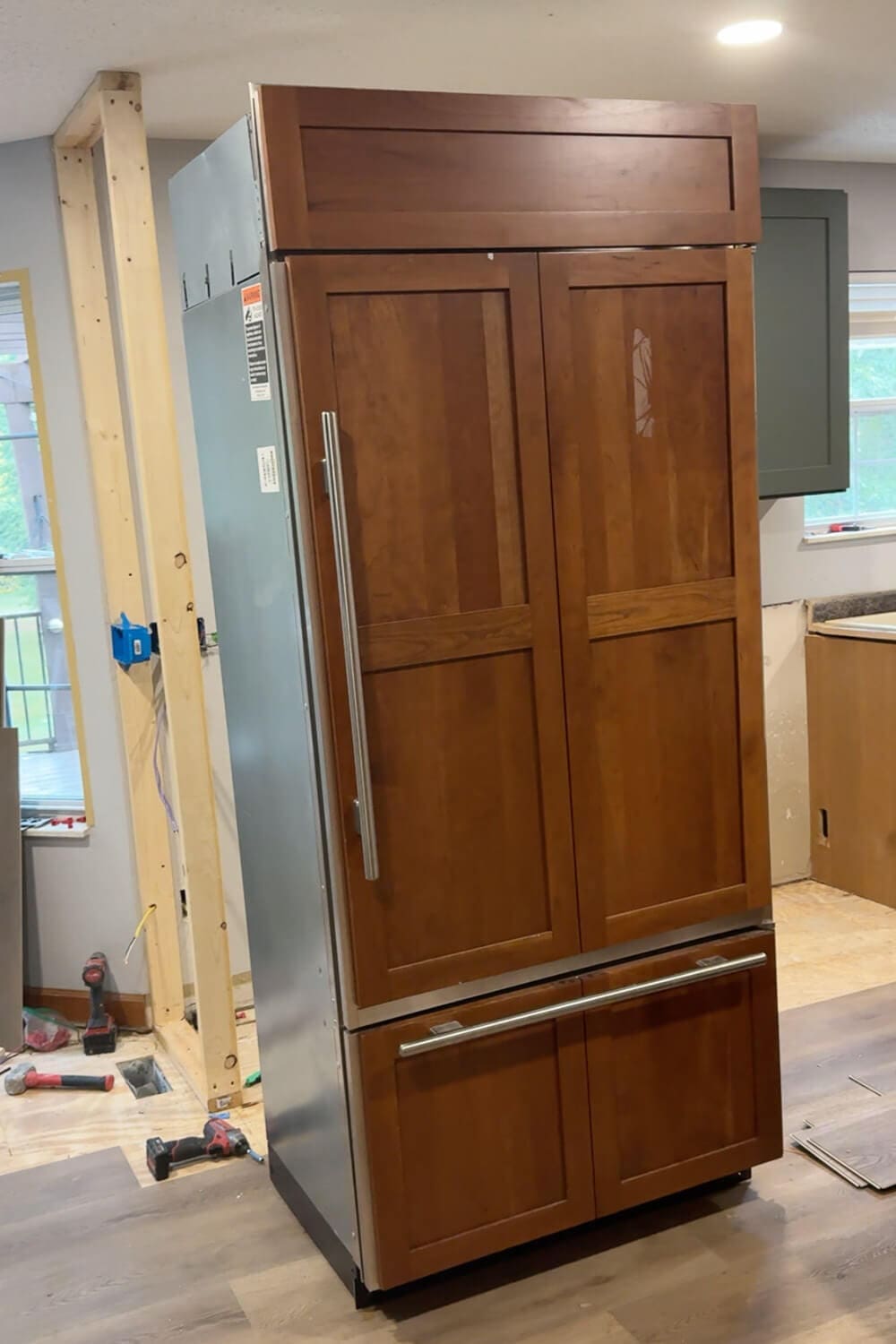 New panel-ready refrigerator set in place during our DIY kitchen remodel, with wood cabinet panels and framing prepped for surrounding cabinets.