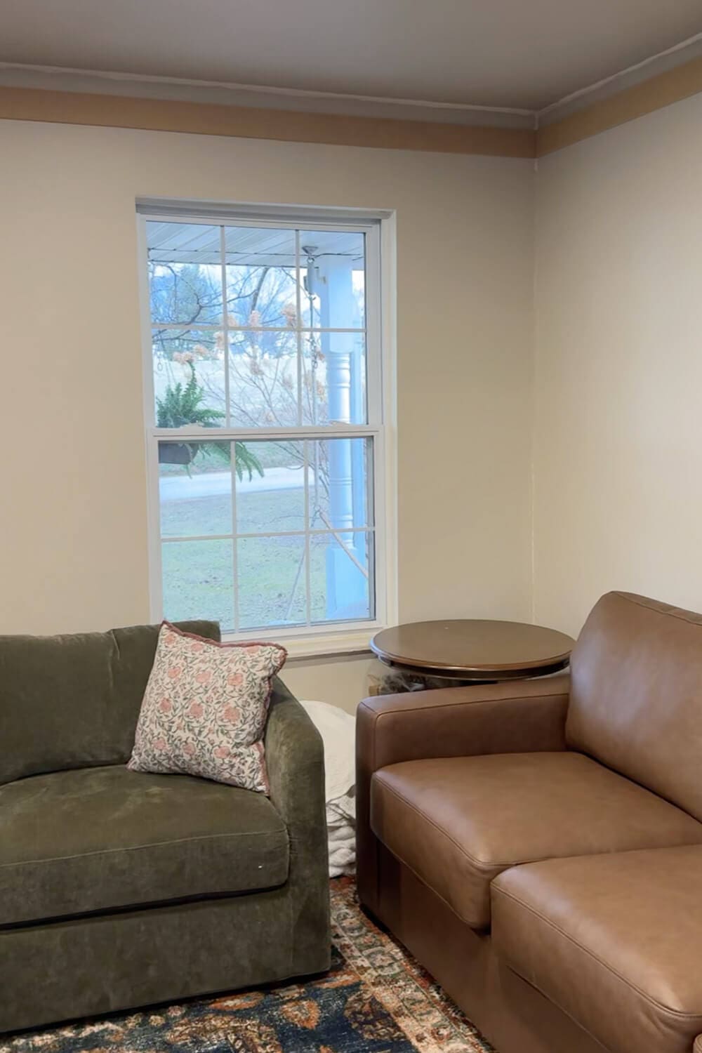 Living room wall with a window where DIY box molding wall trim is started but not finished yet, showing the top trim band in place above a green chair and brown leather sofa.