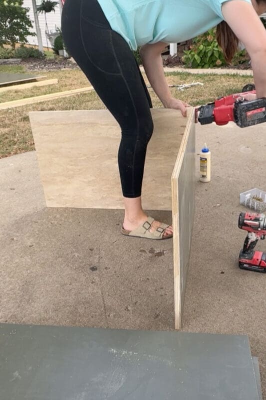 Assembling a plywood bookshelf box on the driveway using a nail gun and wood glue, building the cabinet sections for our DIY built-in bookshelves and home library.