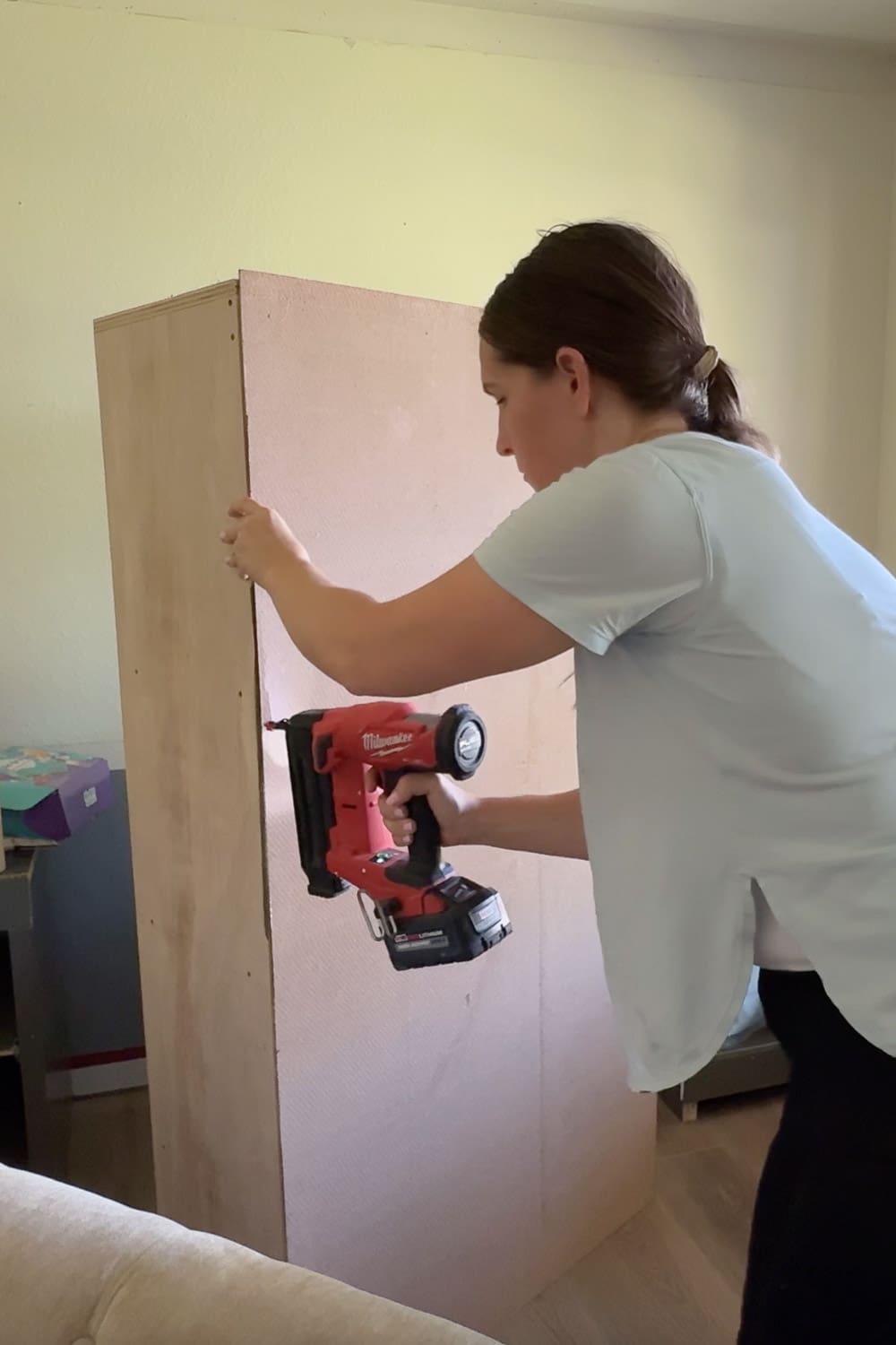 Attaching the backing panel to the DIY bookshelf with a brad nailer to finish the home library shelving unit.