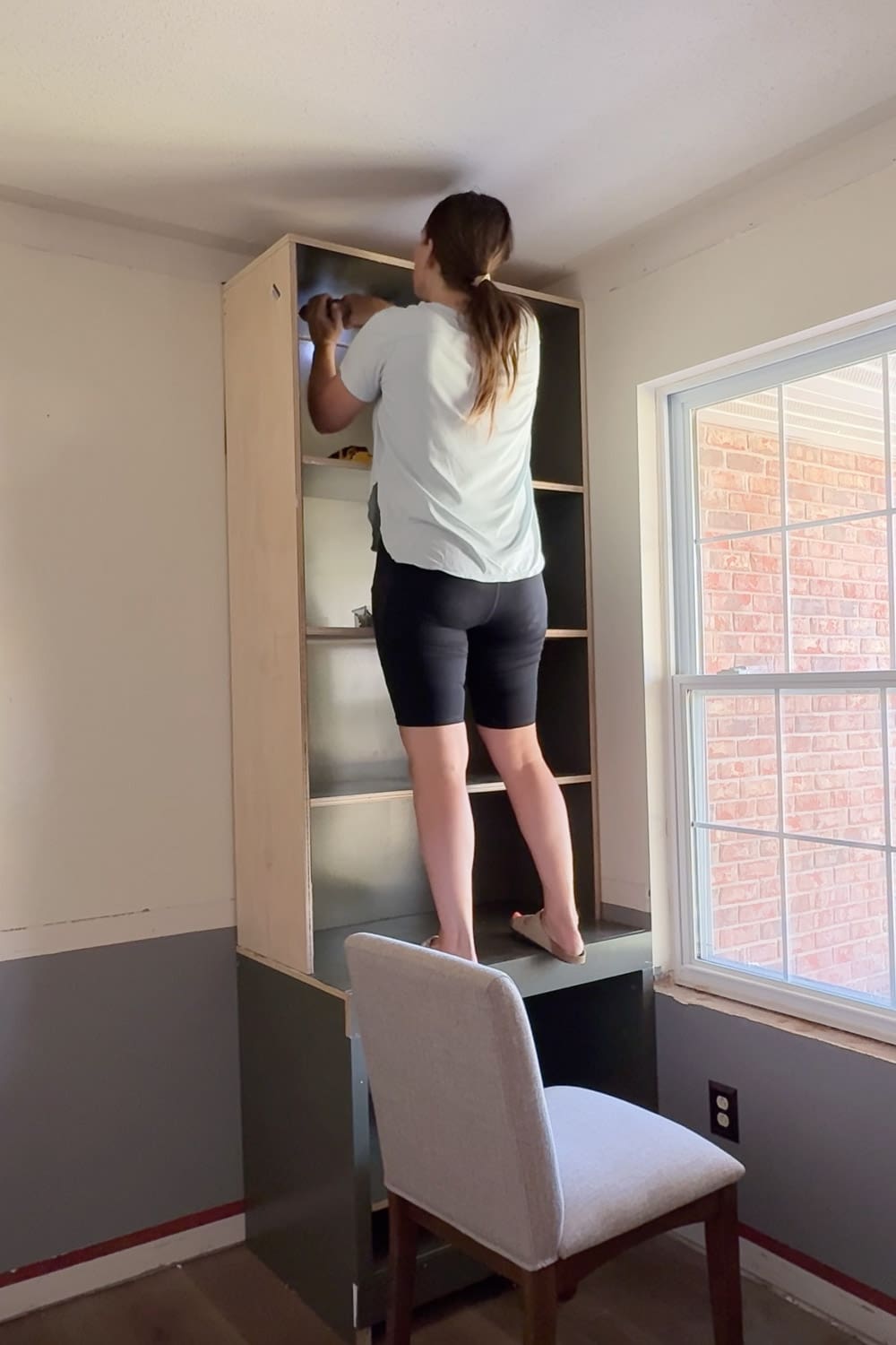 Securing the upper bookshelf unit to the wall above the base cabinet while building custom DIY bookshelves for a home library.