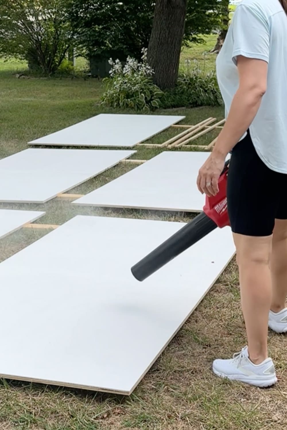 Using a leaf blower to remove sanding dust from primed plywood boards before painting and assembling our DIY bookcases for a home library.