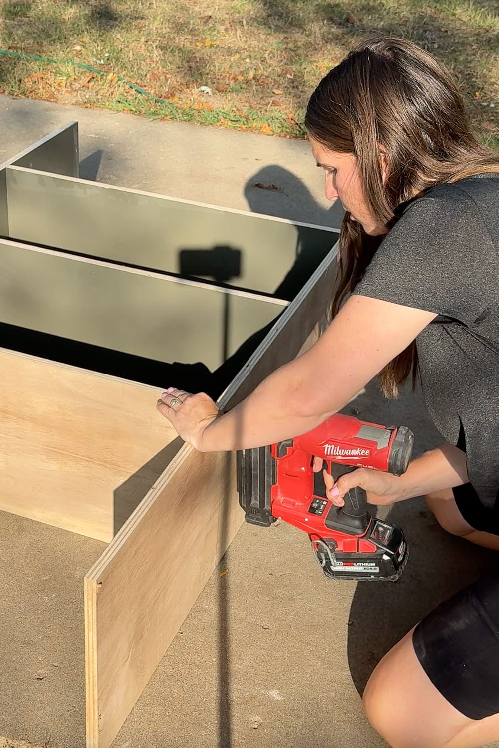 Attaching a plywood bookshelf panel with a brad nailer while assembling DIY home library bookshelves.