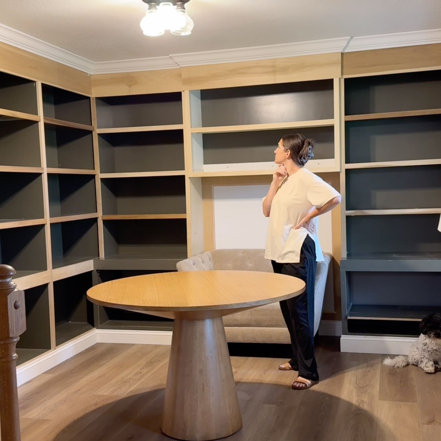 Crystel standing in the empty home library with a hand on her hip, looking up at the finished DIY built-in bookshelves and thinking through what still needs trim, paint, and cabinet doors.