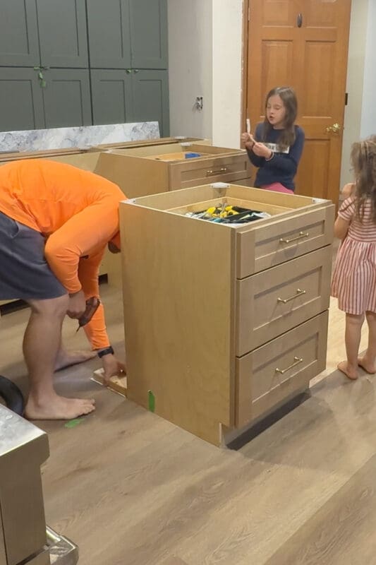 Countertop install step showing 2x4 blocking fastened to the subfloor so the cabinets can be set on top and secured, with drawer cabinets staged nearby.