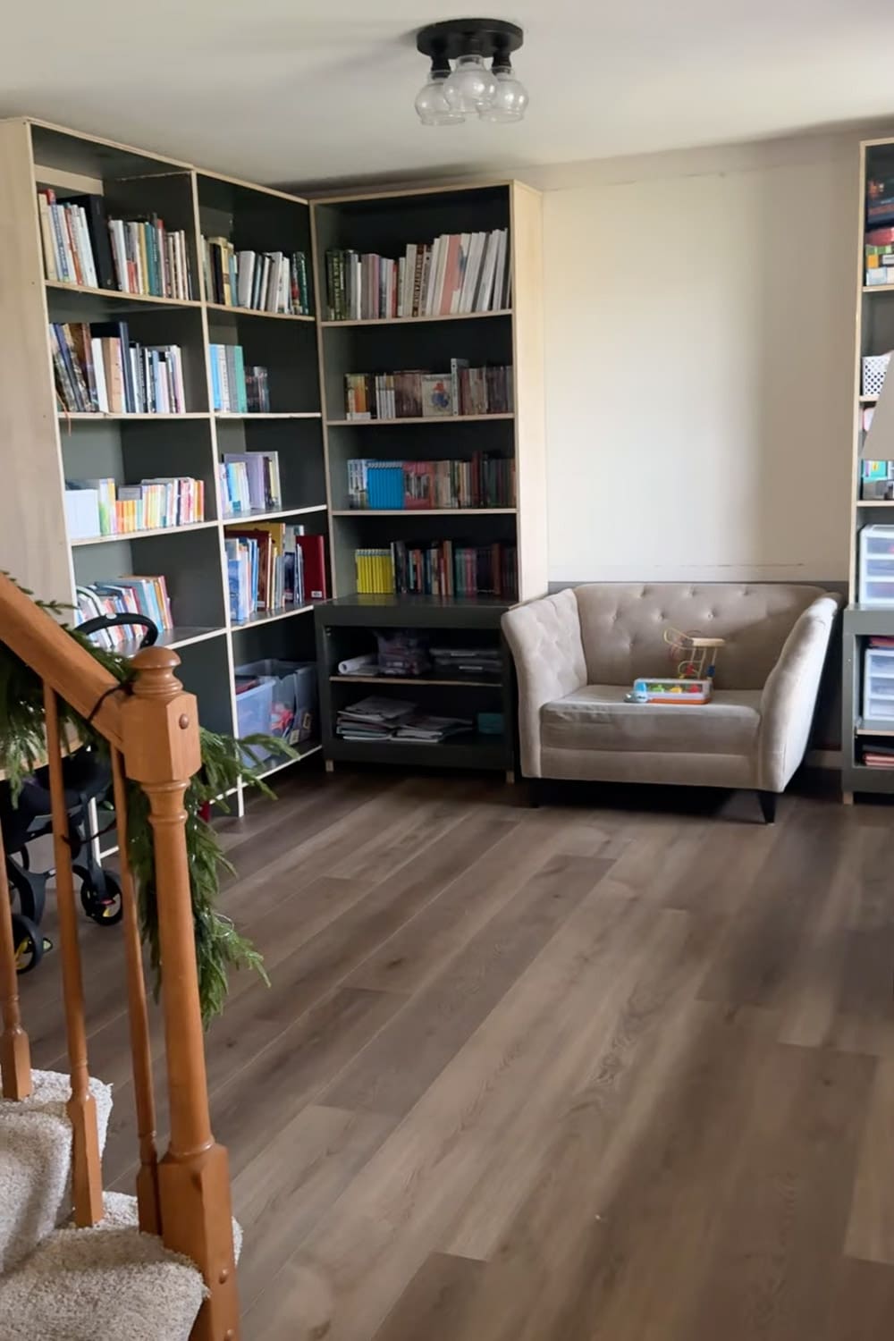 Progress shot of floor-to-ceiling built-in bookshelves in our dining room turned home library, showing the corner shelving layout, dark shelf backs, and a reading chair before the built-ins are trimmed and painted.