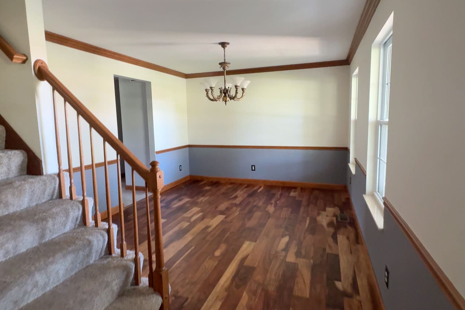 Before photo of our formal dining room with hardwood floors, gray wainscoting, wood trim, and a brass chandelier, showing the empty space before we started to swap it for a cozy home library.