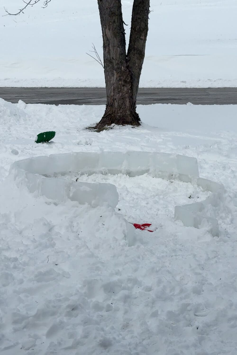 First rows of clear ice blocks stacked in a circle to start the base of a backyard igloo, showing the lower levels before building the dome for a how to build an igloo tutorial