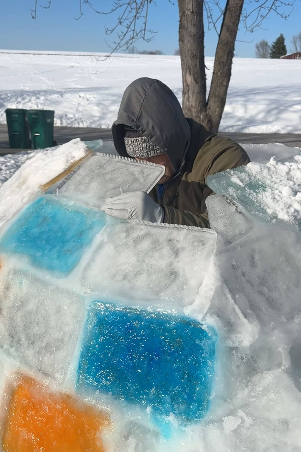 Close-up of stacking and fitting ice blocks to build an igloo wall, showing colored ice panels and snow packed between blocks for a how to build an igloo step-by-step