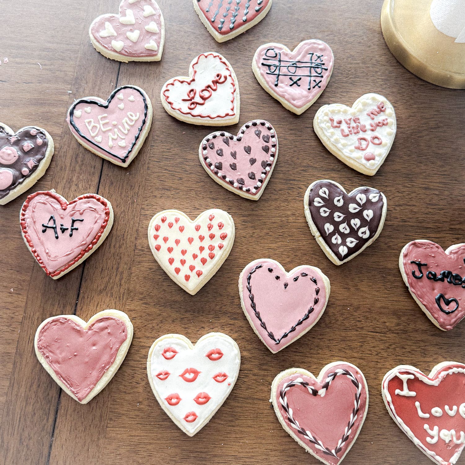 Valentine heart sugar cookies decorated with pink and white royal icing without meringue powder, featuring piped sayings, patterns, and details on a wooden table.