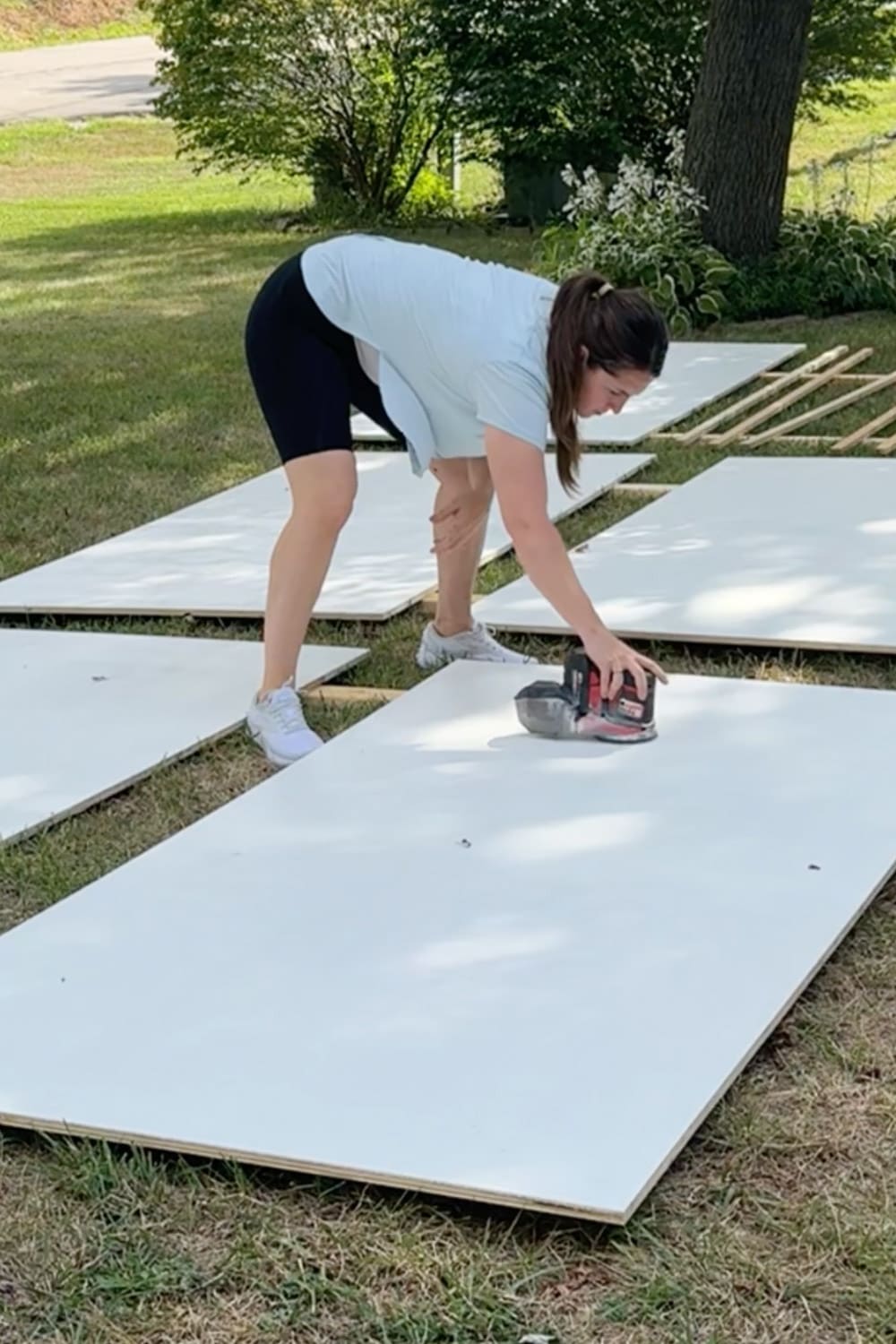 Sanding primed plywood panels outside with an orbital sander to prep smooth boards for painted DIY bookcases in our cozy home library.