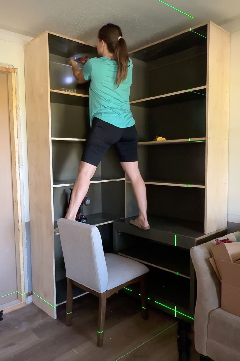 Attaching a tall DIY bookcase to the wall using a laser level while building custom home library built-ins.