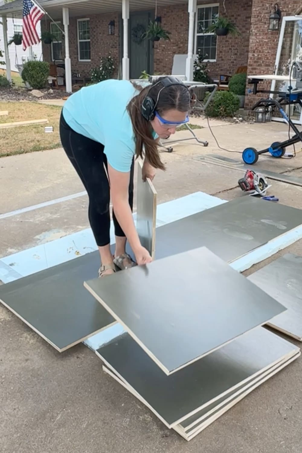 Stacking and flipping freshly painted plywood panels on the driveway to dry, prepping the pieces for our DIY built-in bookshelves and home library wall.