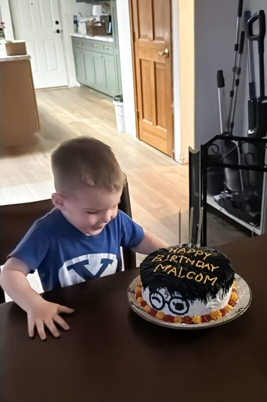 young boy celebrating with harry potter birthday cake with glasses design and name malcom written on top