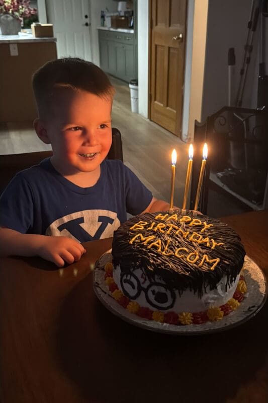 young boy smiling at harry potter birthday cake with black frosting top and candles lit