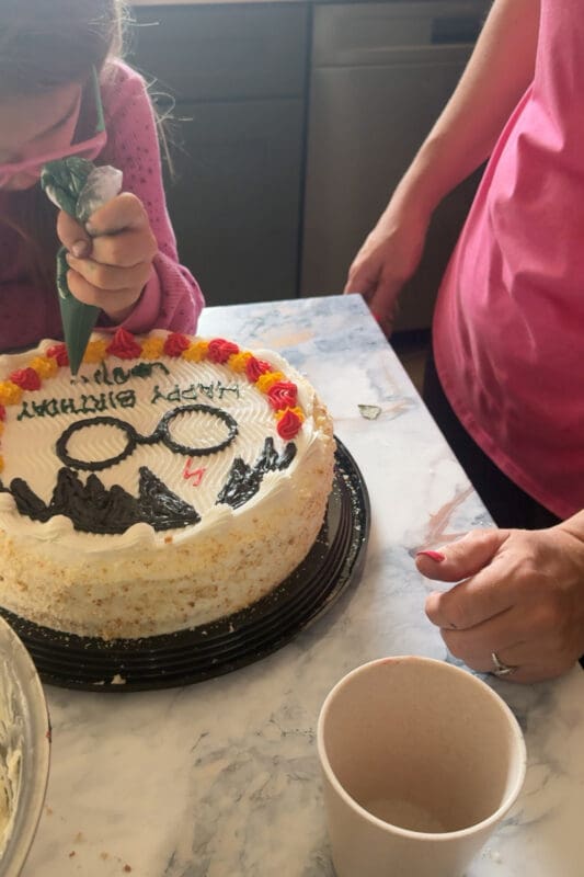 child piping green frosting to help decorate harry potter cake birthday message