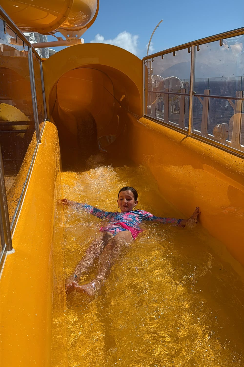 child riding aquamouse waterslide on disney cruise ship with ocean view and bright yellow slide during family cruise