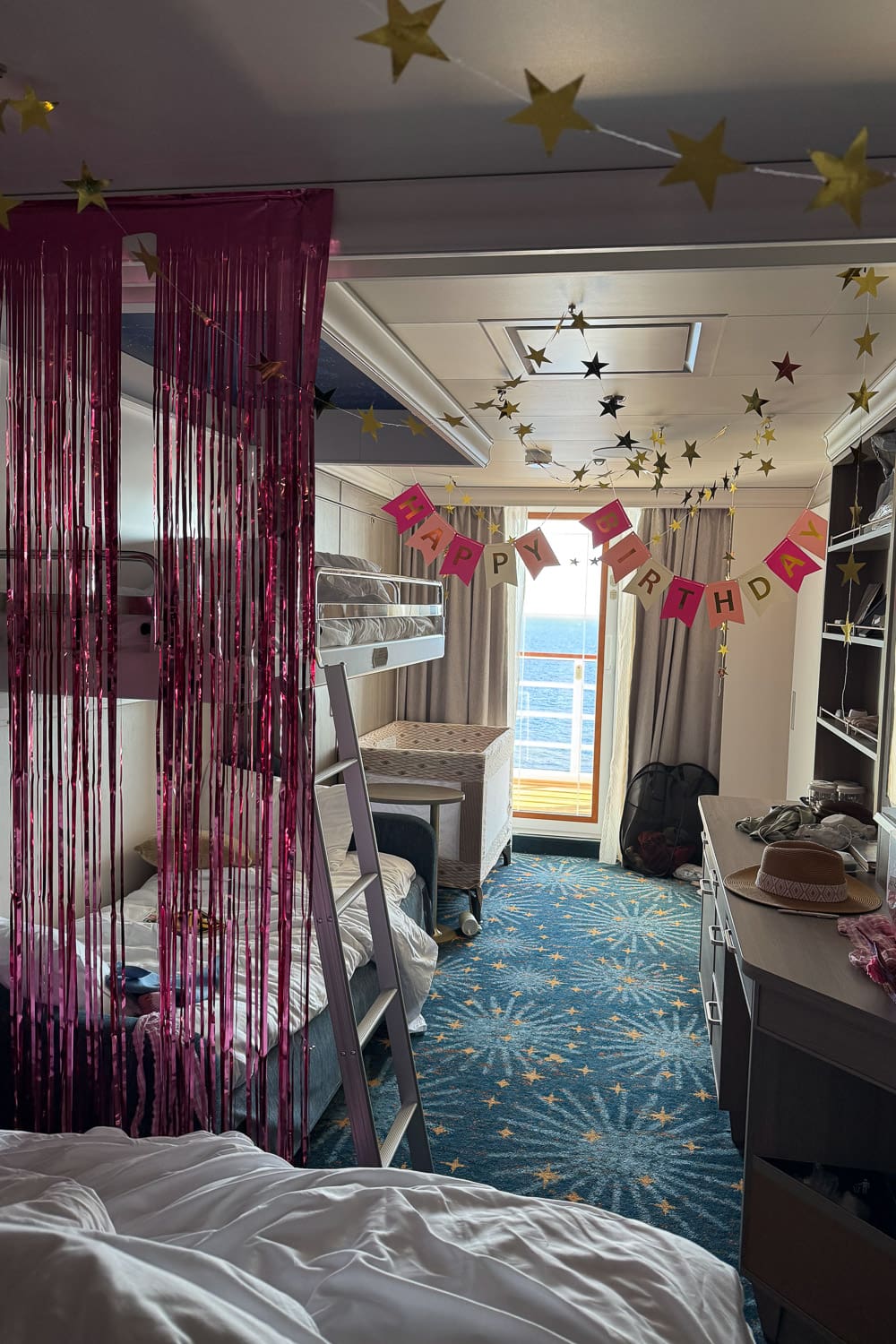 disney cruise stateroom with bunk beds decorated for birthday with banner, streamers, and ocean view balcony for family cruise with kids