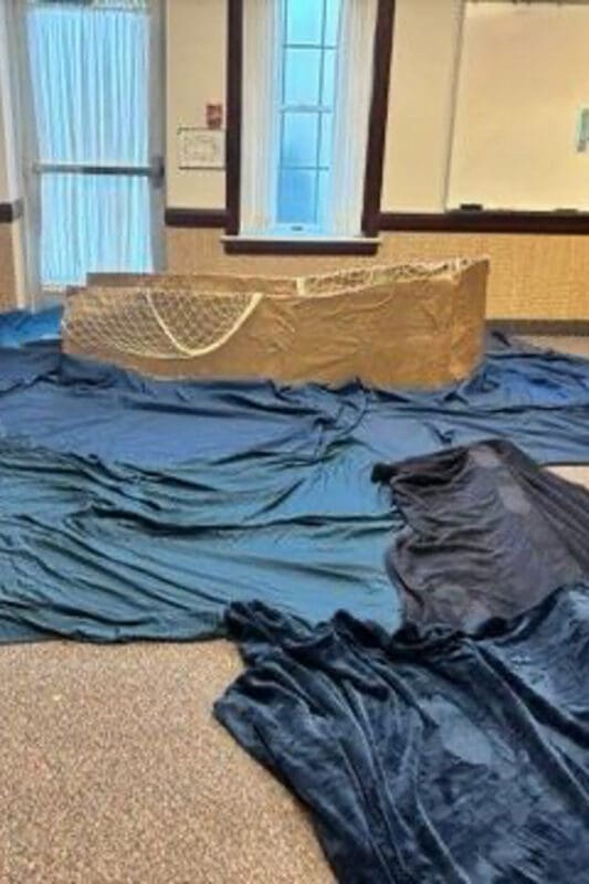 DIY water and boat setup for an Easter church activity for kids representing Jesus walking on water with blue fabric and simple props