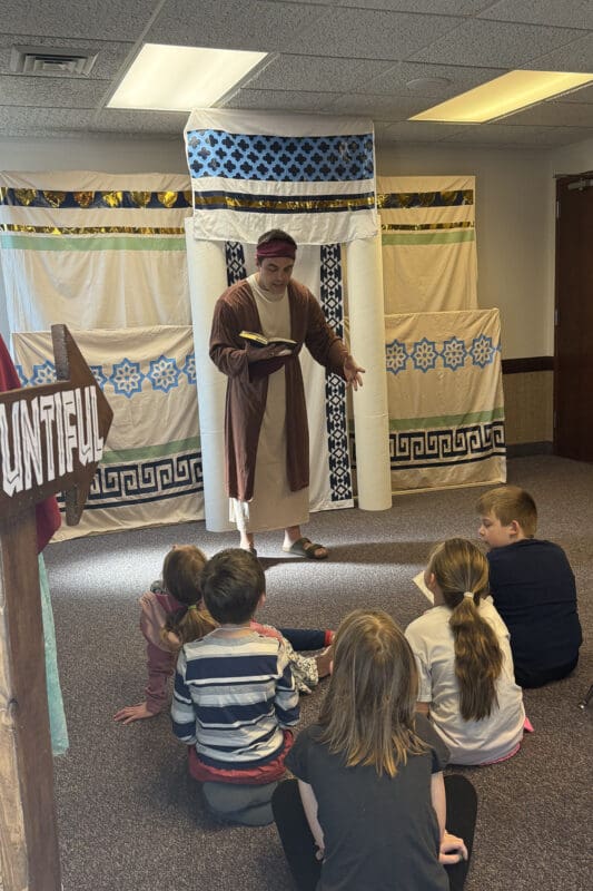 Volunteer dressed in biblical costume teaching children from the scriptures during an Easter church activity for kids interactive station