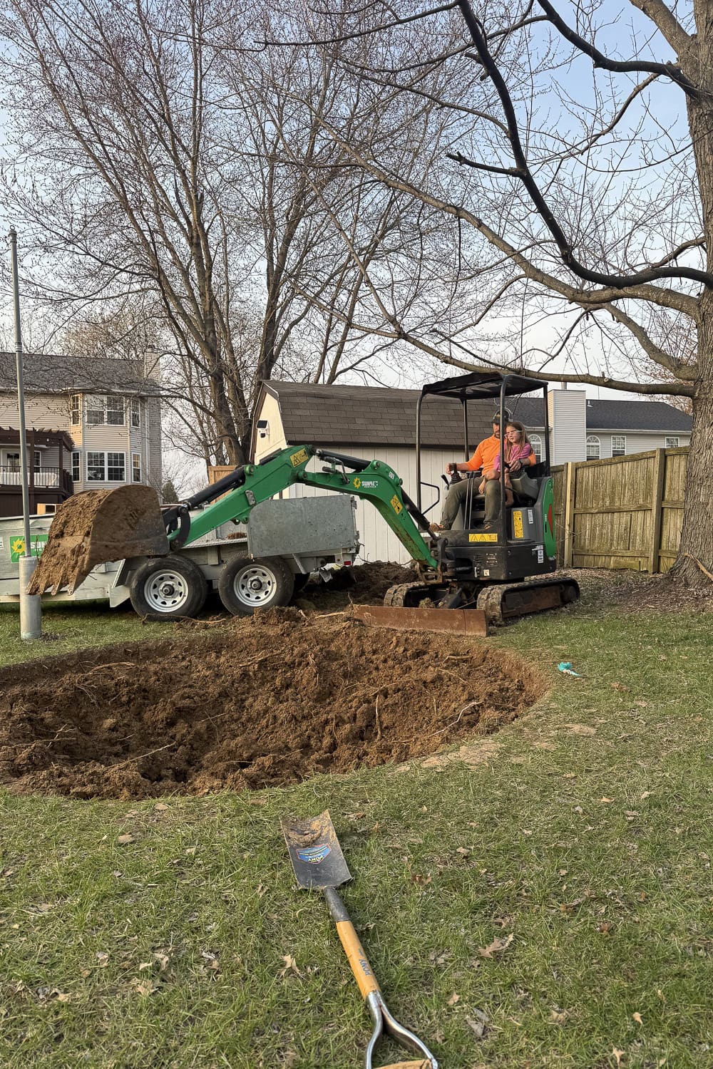 Using an excavator to dig an in-ground trampoline hole and load dirt into a dump trailer in the backyard